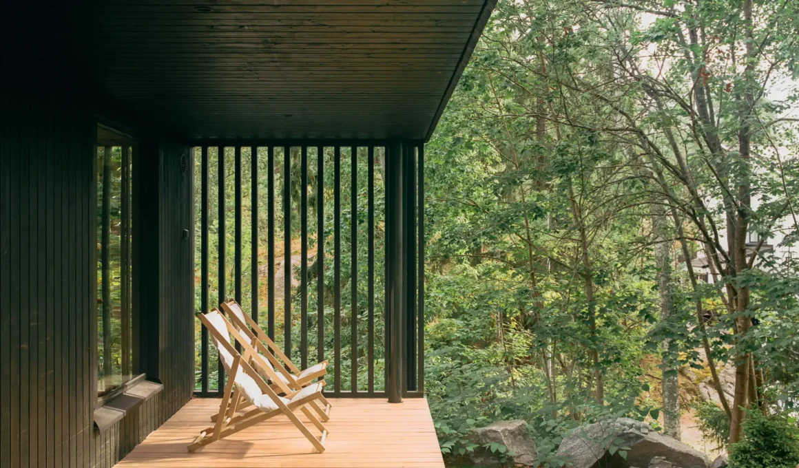 Talli Villa Margo Helsinki sheltered terrace, dark green vertical boarding, timber deck, folding chairs, preserved vegetation and exposed granite boulders