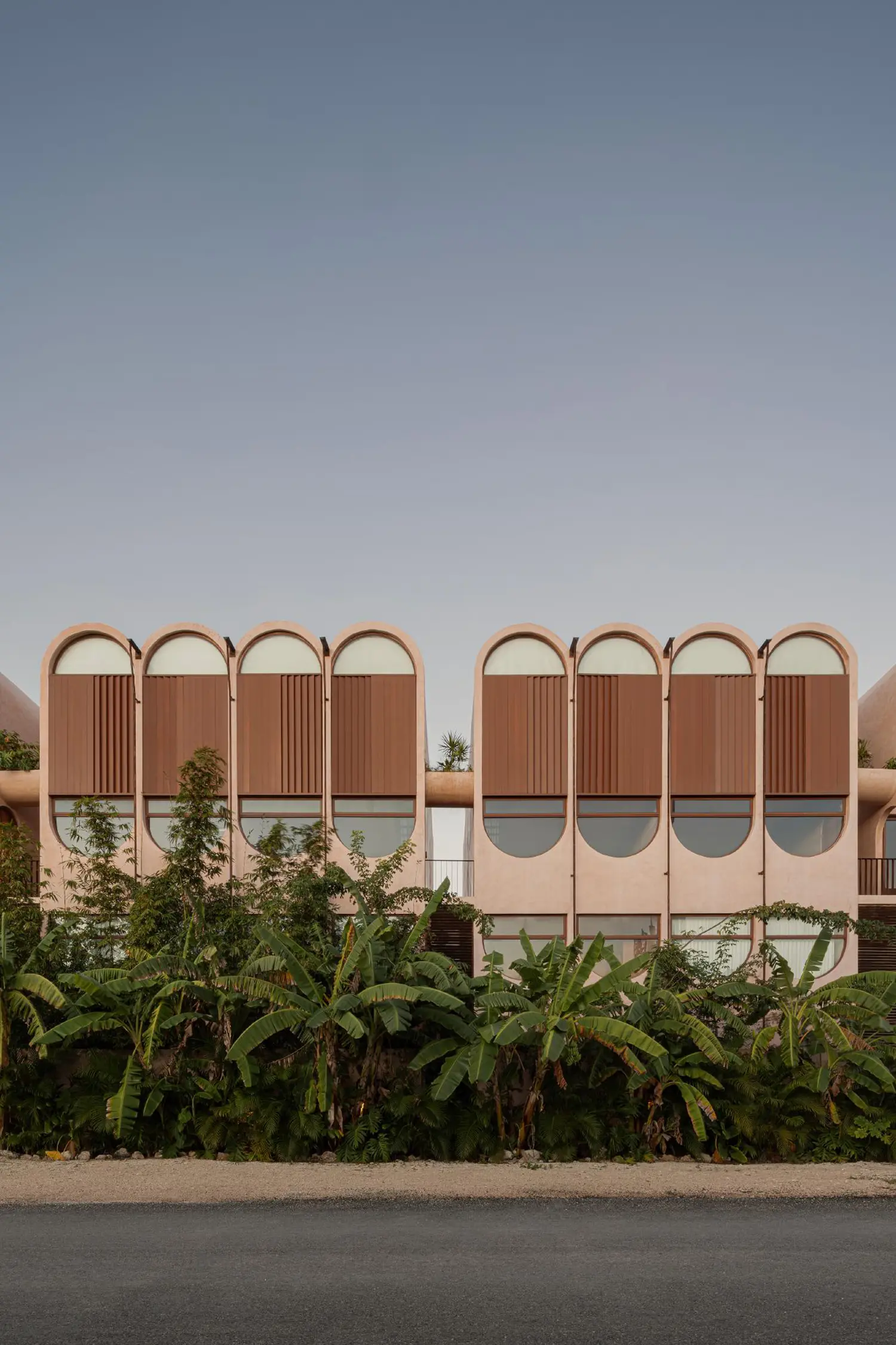 Exterior facade of Babel featuring repetitive pink arches and dark wooden louvers above tropical greenery.
