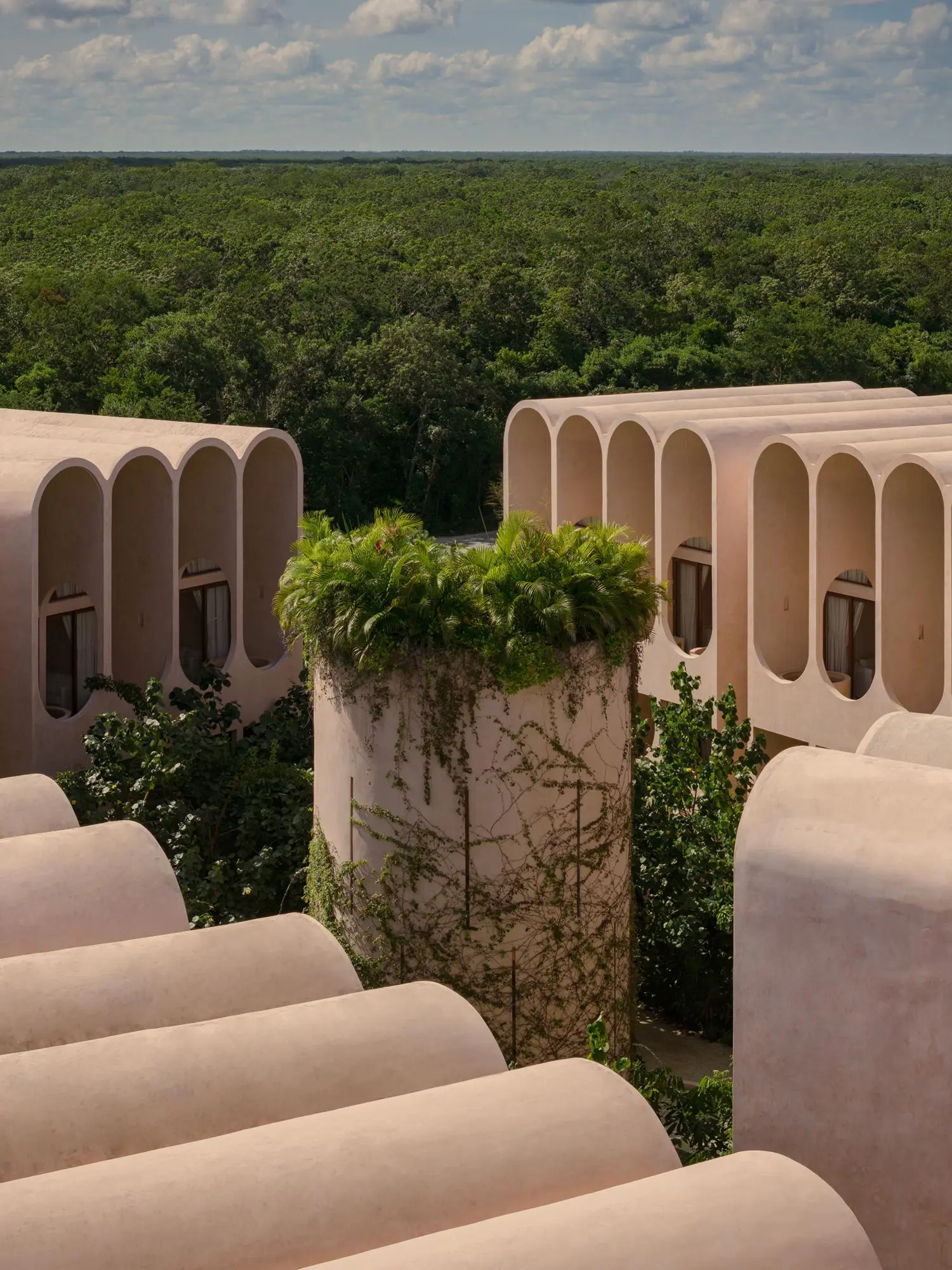 Perspective view of arched rooftops and a central vegetation-topped tower overlooking the Mayan jungle.