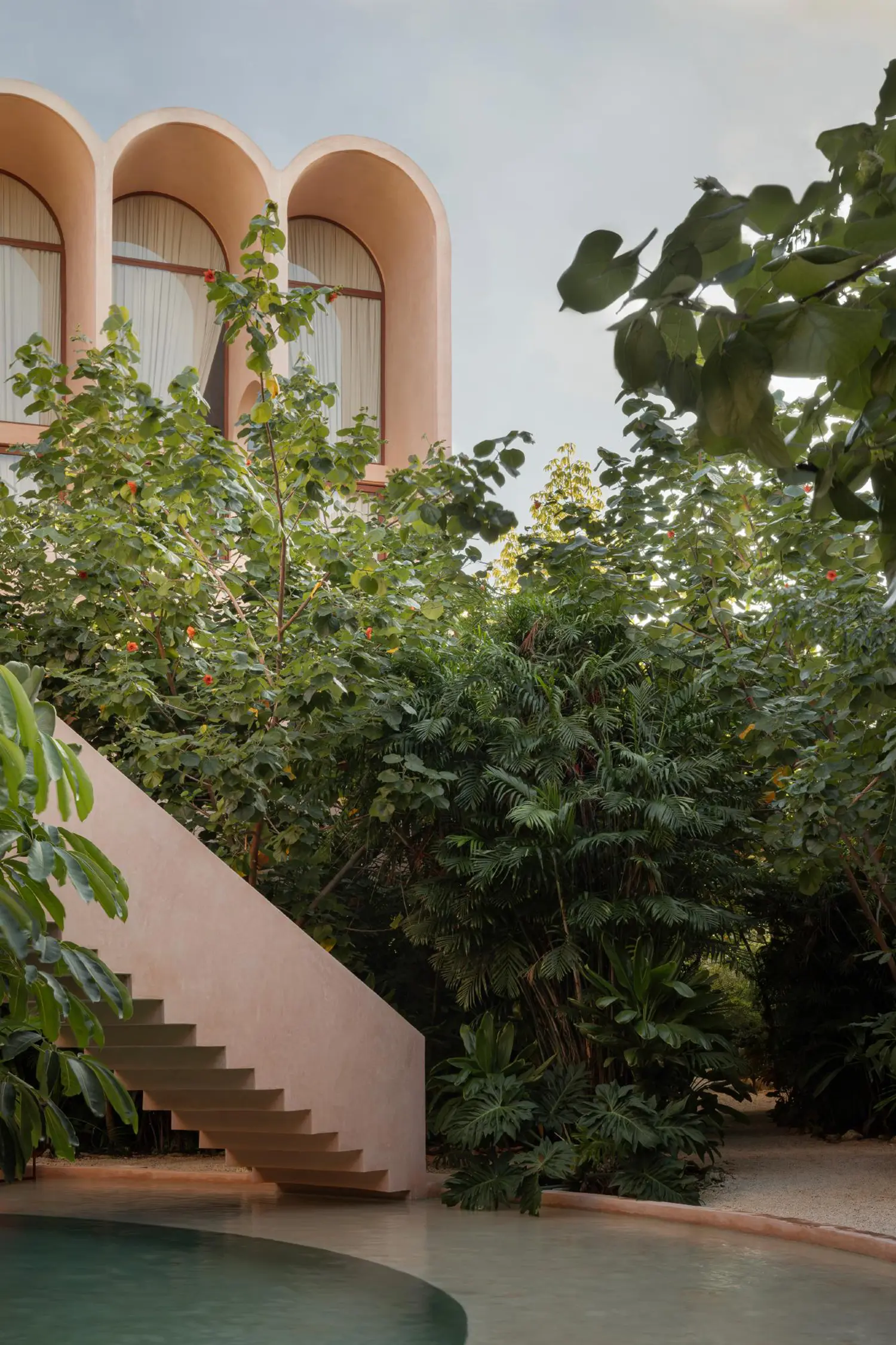 A concrete staircase leads through dense tropical plants toward a high-arched residential unit.