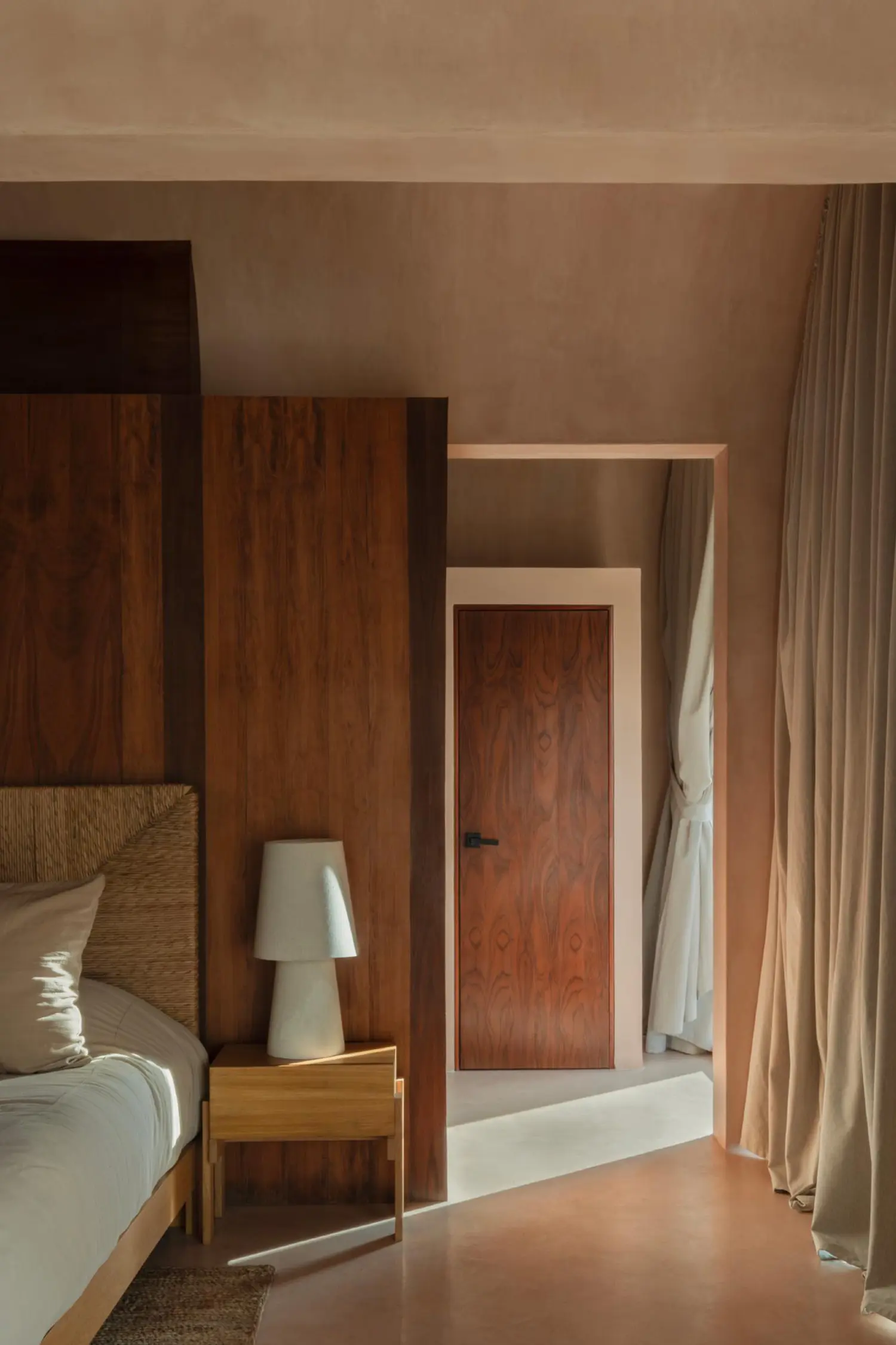 Bedroom interior featuring a wooden headboard, tropical wood door, and a glimpse of the jungle through a window.