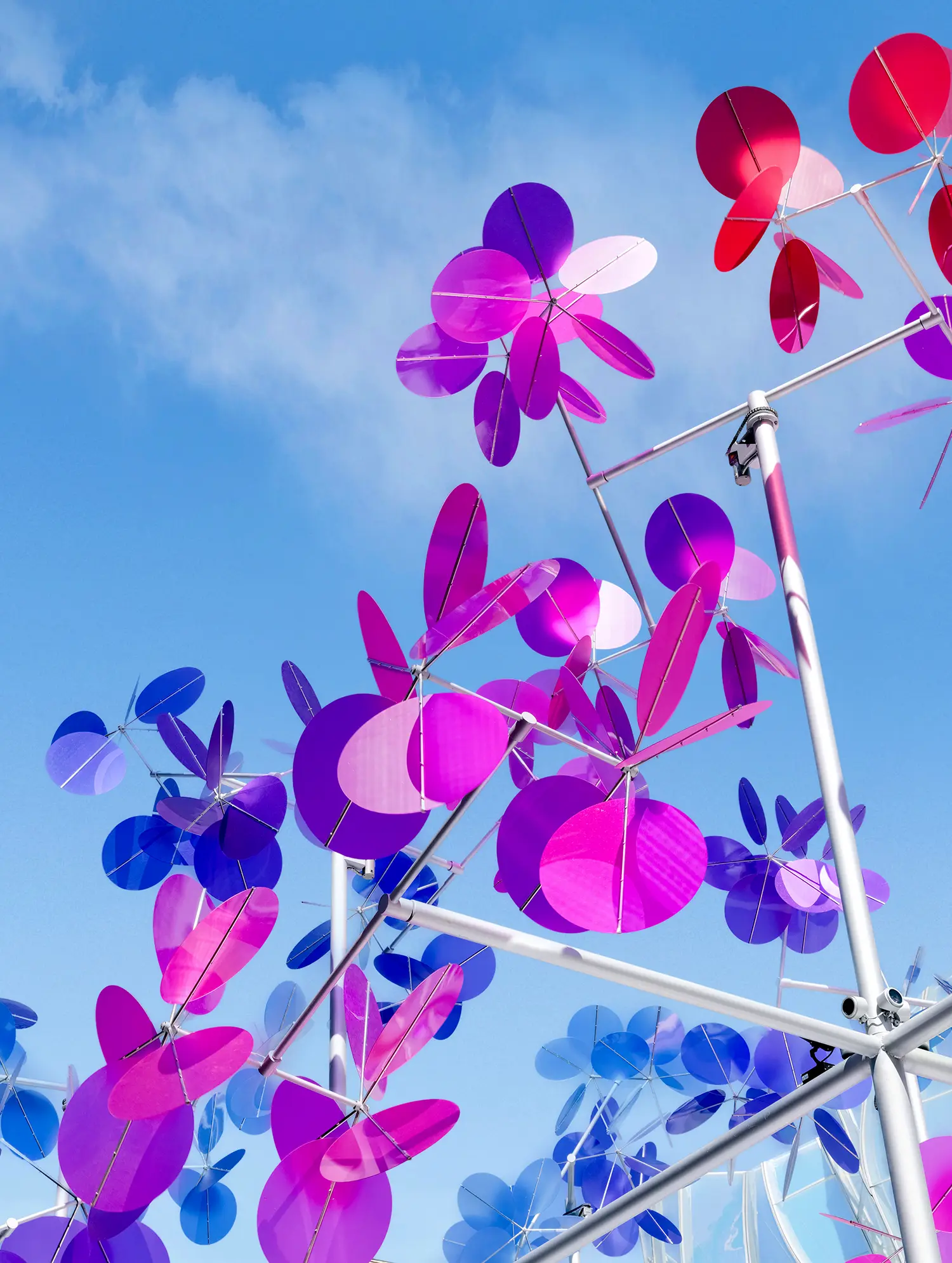 Low-angle close-up of Vincent Leroy Point Cloud installation showing purple, magenta, and blue translucent circular plates attached to a metallic framework against a clear blue sky.