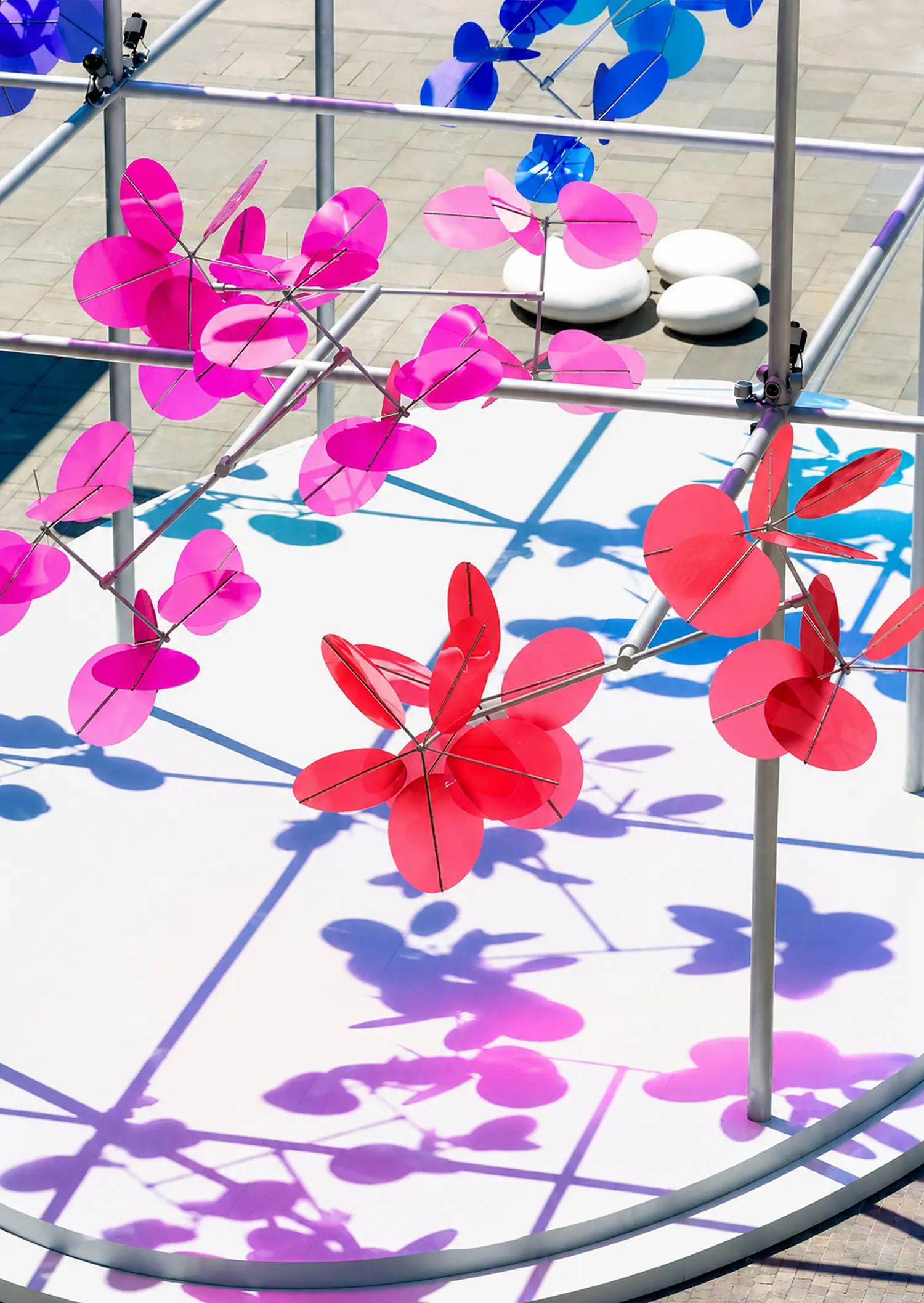 Elevated close-up of Vincent Leroy Point Cloud kinetic sculpture showing red and pink discs casting sharp magenta and purple shadows onto a white platform.