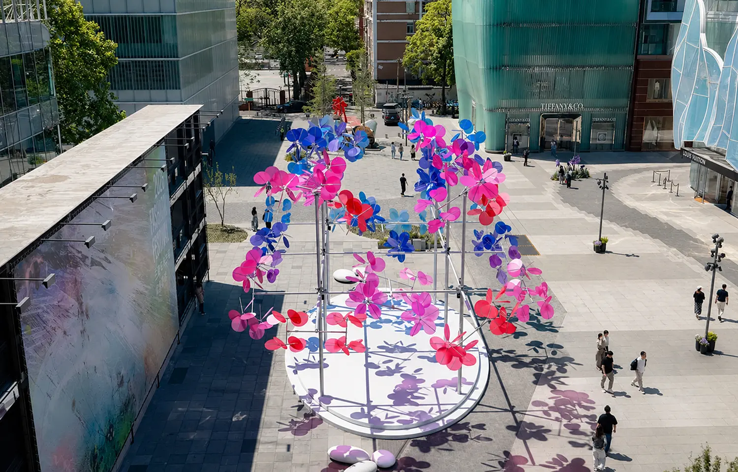 High-angle wide view of Vincent Leroy Point Cloud installation in a Beijing public plaza, showcasing its oval base, metal structure, and long colored shadows cast across the pavement.