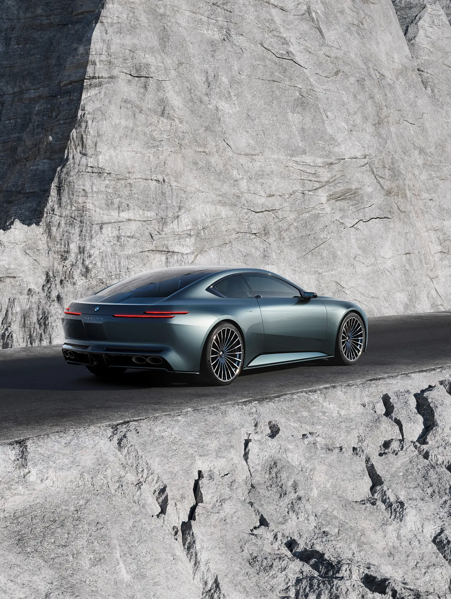 Rear quarter view of the Vision BMW ALPINA coupe on a mountain road next to a massive vertical rock formation.