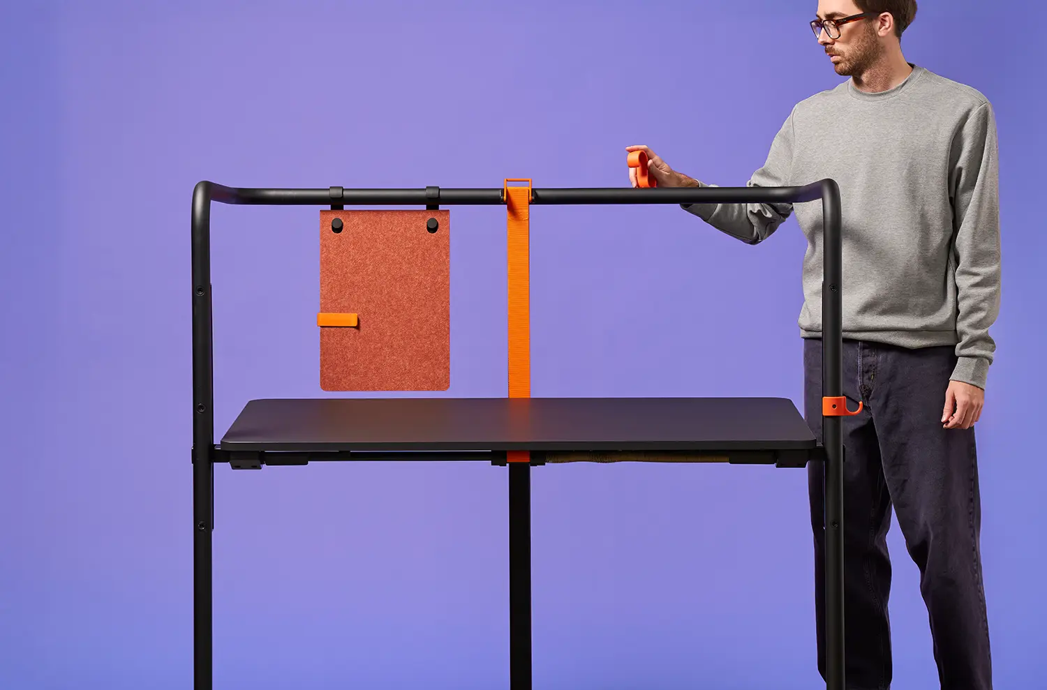 A man interacting with a Scout desk by attaching an orange hook to the black tubular frame.