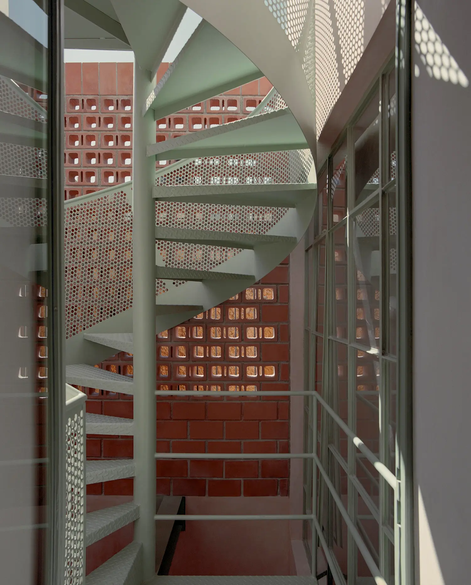 Casa Xoltic AMASA Estudio, cantilevered green steel spiral staircase, perforated steel treads, brick lattice screen backdrop, Coyoacán