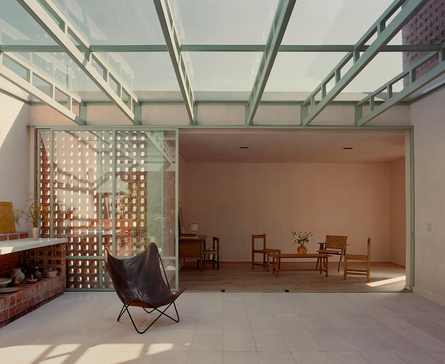 Casa Xoltic AMASA Estudio, first floor patio with green steel and glass pergola, brick lattice screen, pink chukum interior wall visible, Coyoacán