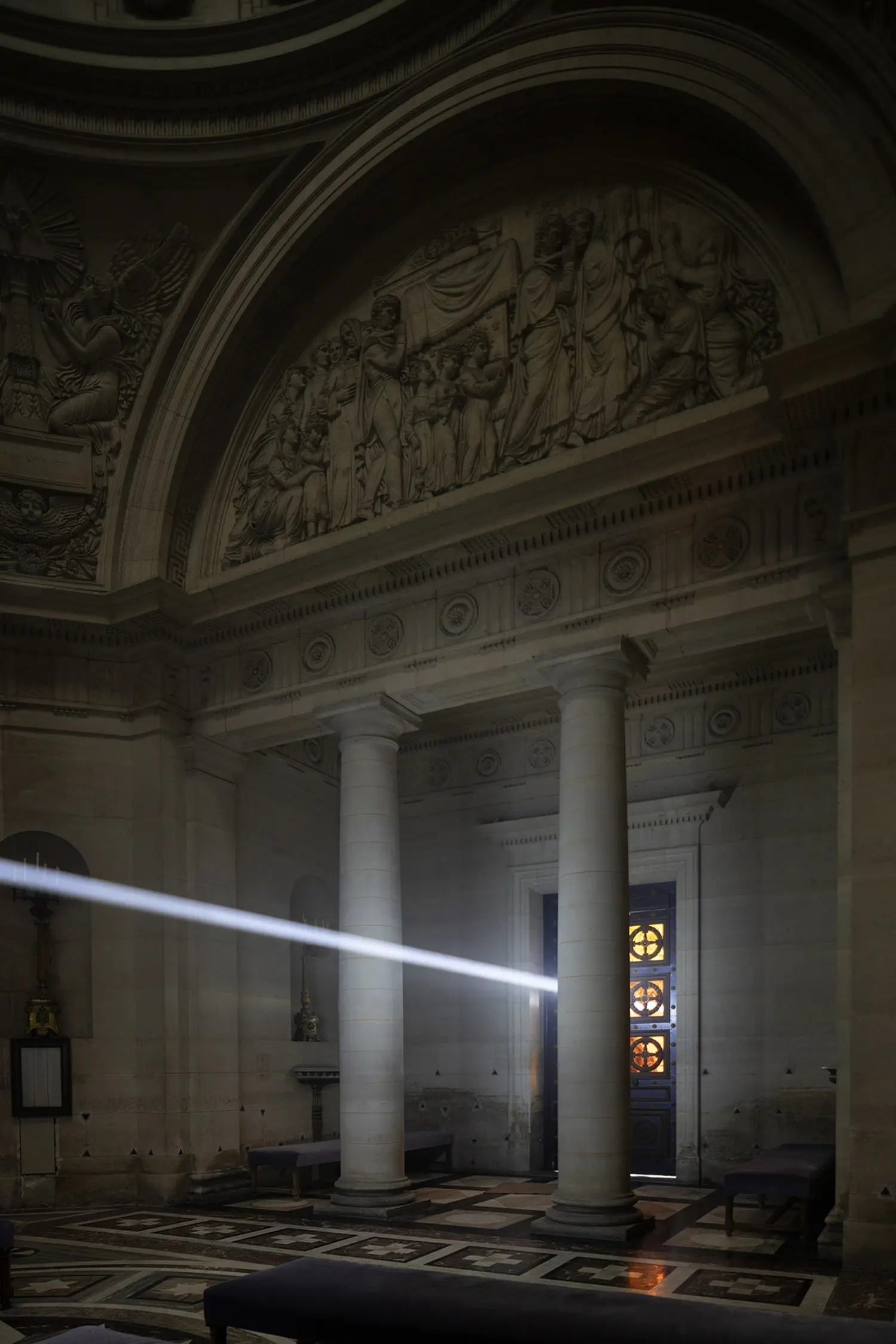 Threshold Emilio Ferro, white light beam extending toward open chapel entrance doors, neoclassical colonnade Paris 2026