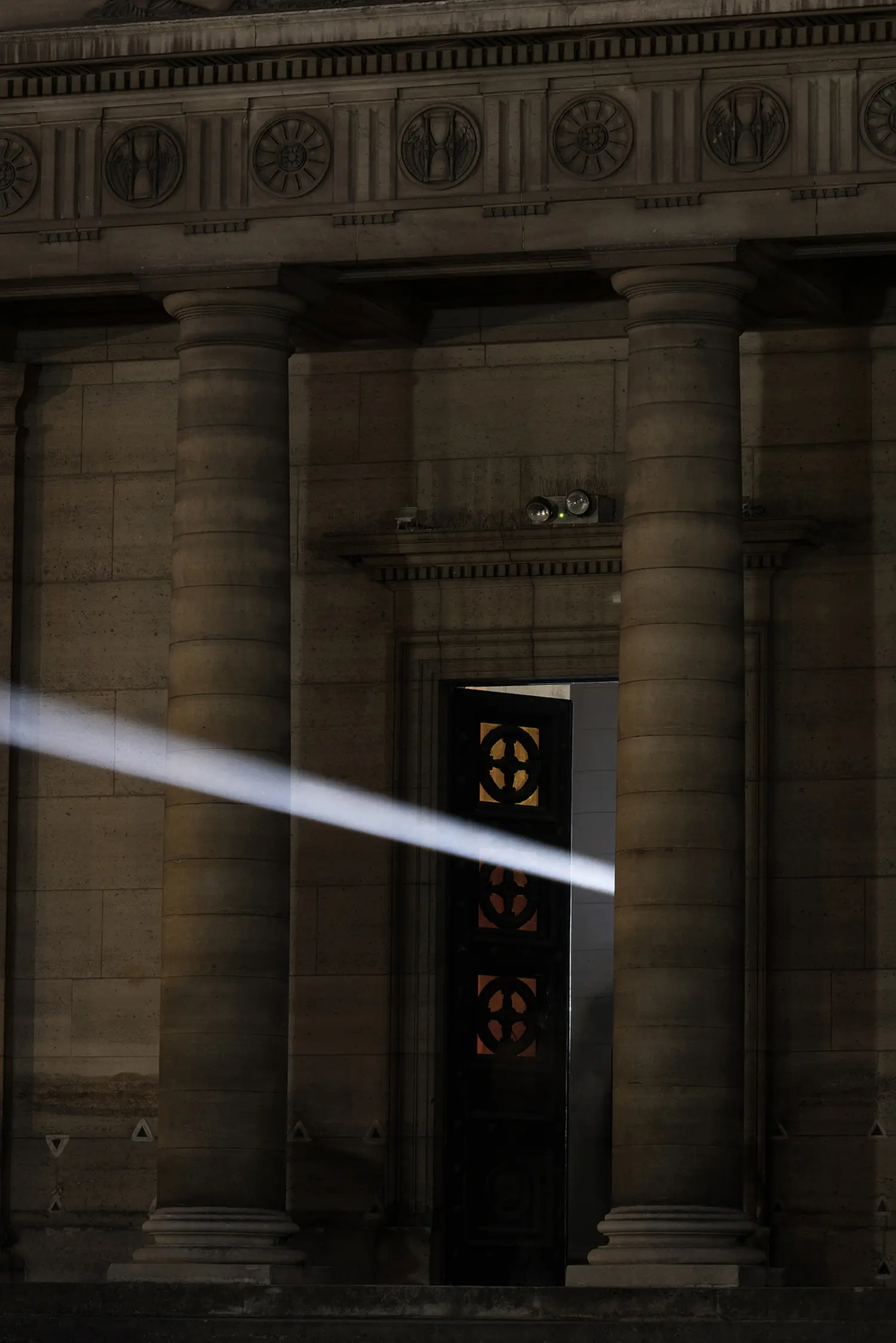 Threshold Emilio Ferro, white light beam exiting through open entrance door of Chapelle Expiatoire, neoclassical stone facade Paris night 2026