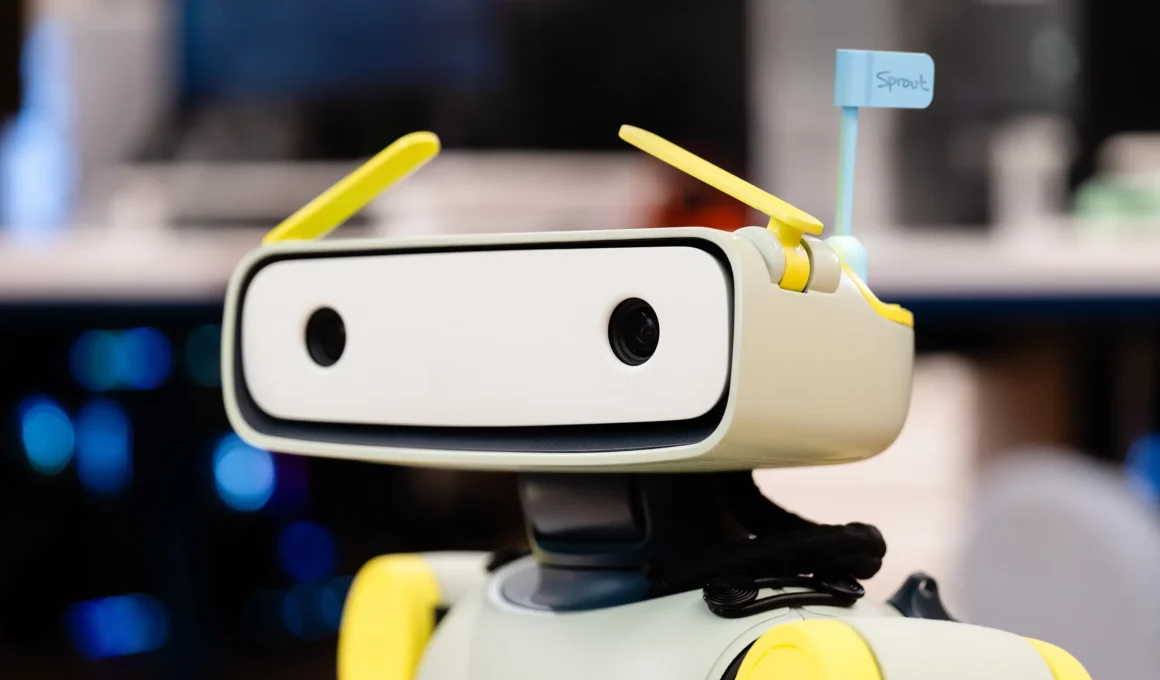 Fauna Robotics Sprout humanoid robot head close-up, rectangular white face panel, two stereo cameras, yellow-green motorized antenna eyebrows, name tag