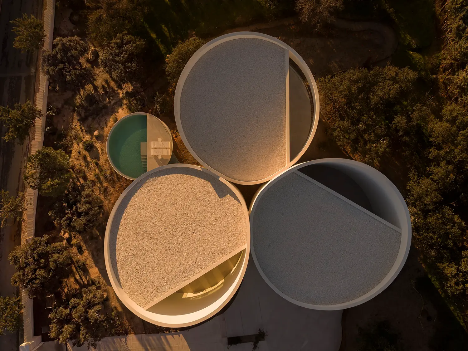 Top-down aerial view of House in Las Rozas at dusk, three circular roof volumes with oblique cuts and adjacent round pool
