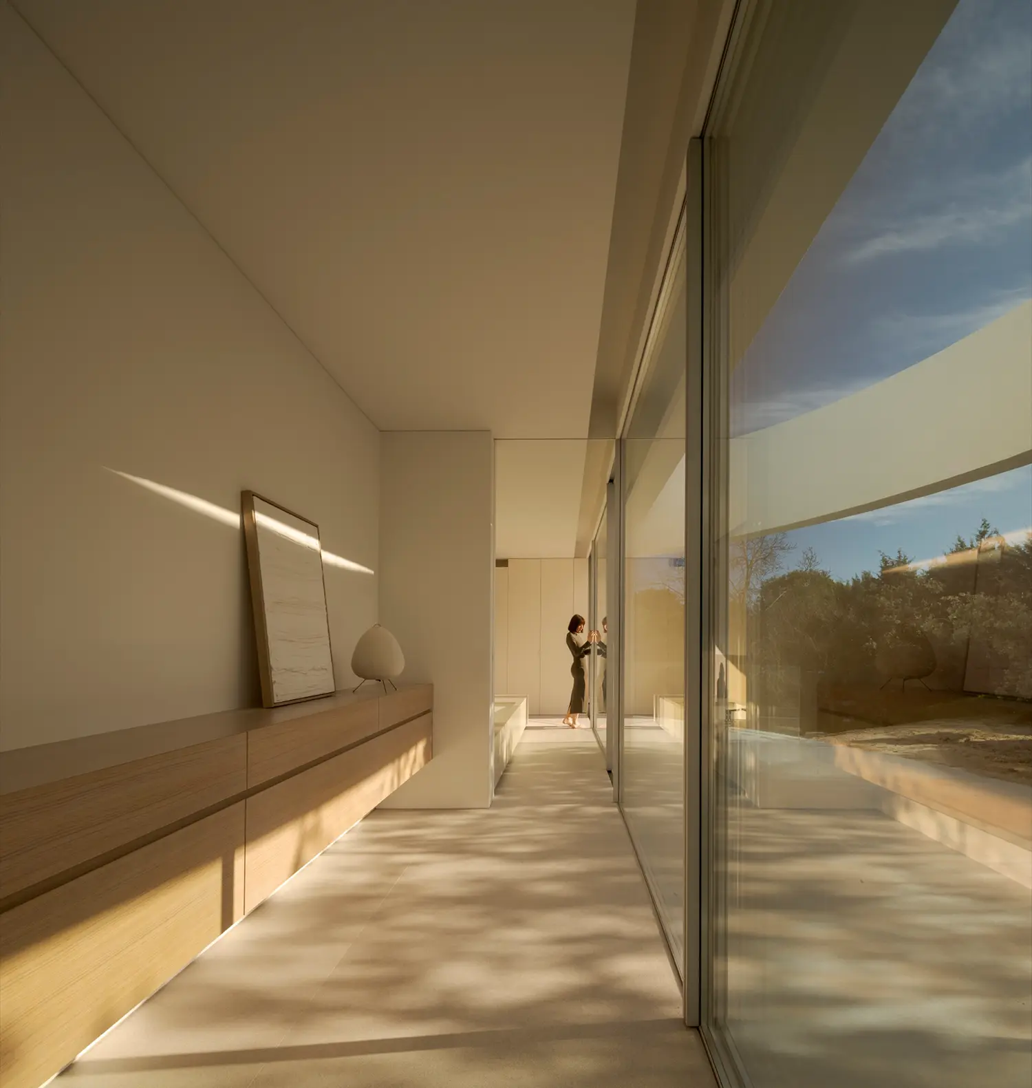 Interior corridor of House in Las Rozas with full-height glass wall, built-in oak cabinetry, and two figures walking toward the threshold