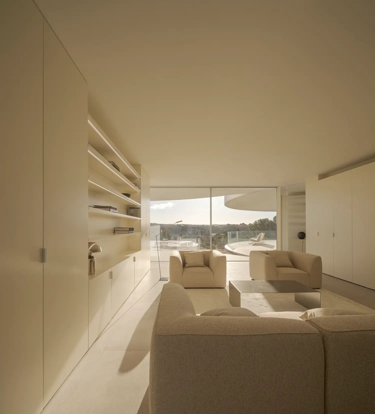 Living room interior of House in Las Rozas with curved upholstered seating, built-in shelving, and panoramic glazing toward landscape