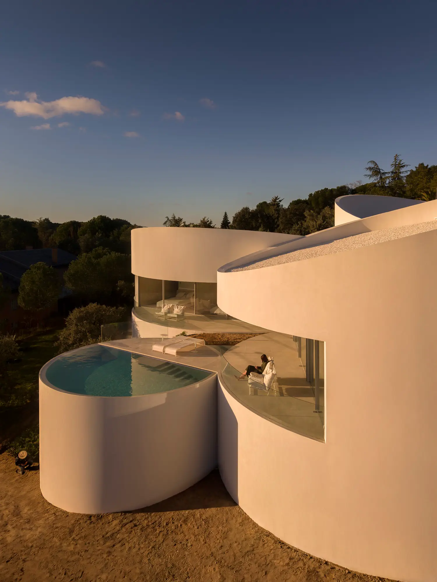 Interior threshold of House in Las Rozas, glass corner window opening onto pool terrace with curved white volume beyond