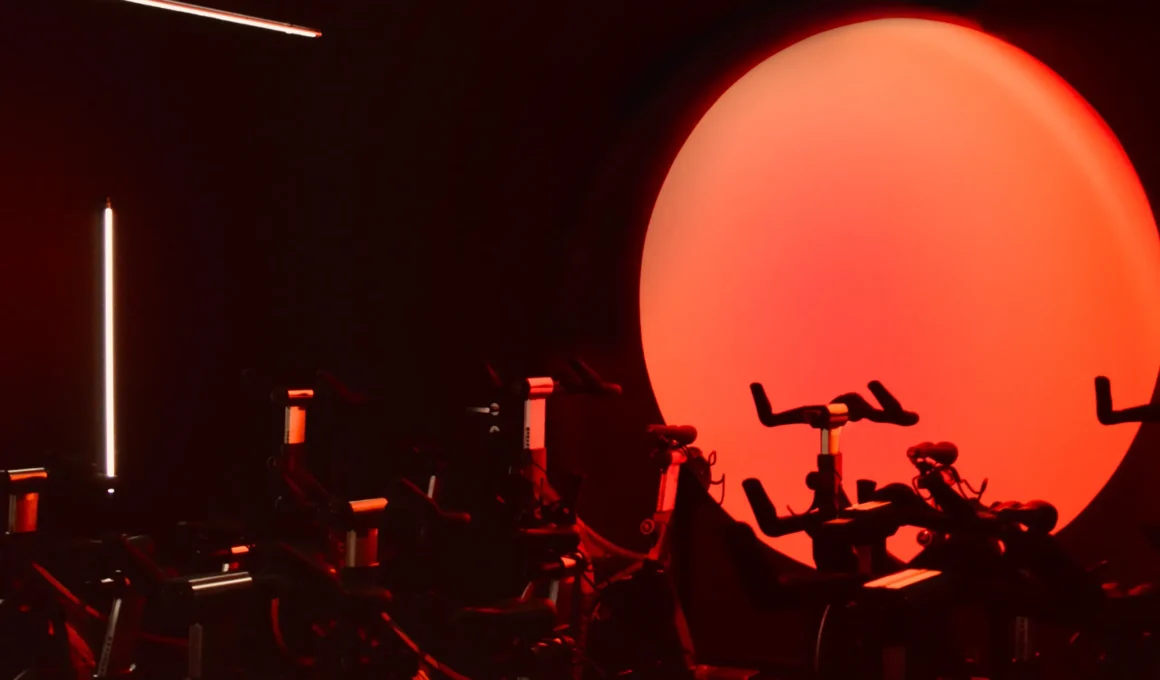 GYRU indoor cycling studio by ON13 Atelier Milan, matte black cycling room, large vermillion circular backlight, LED strip, silhouetted bikes
