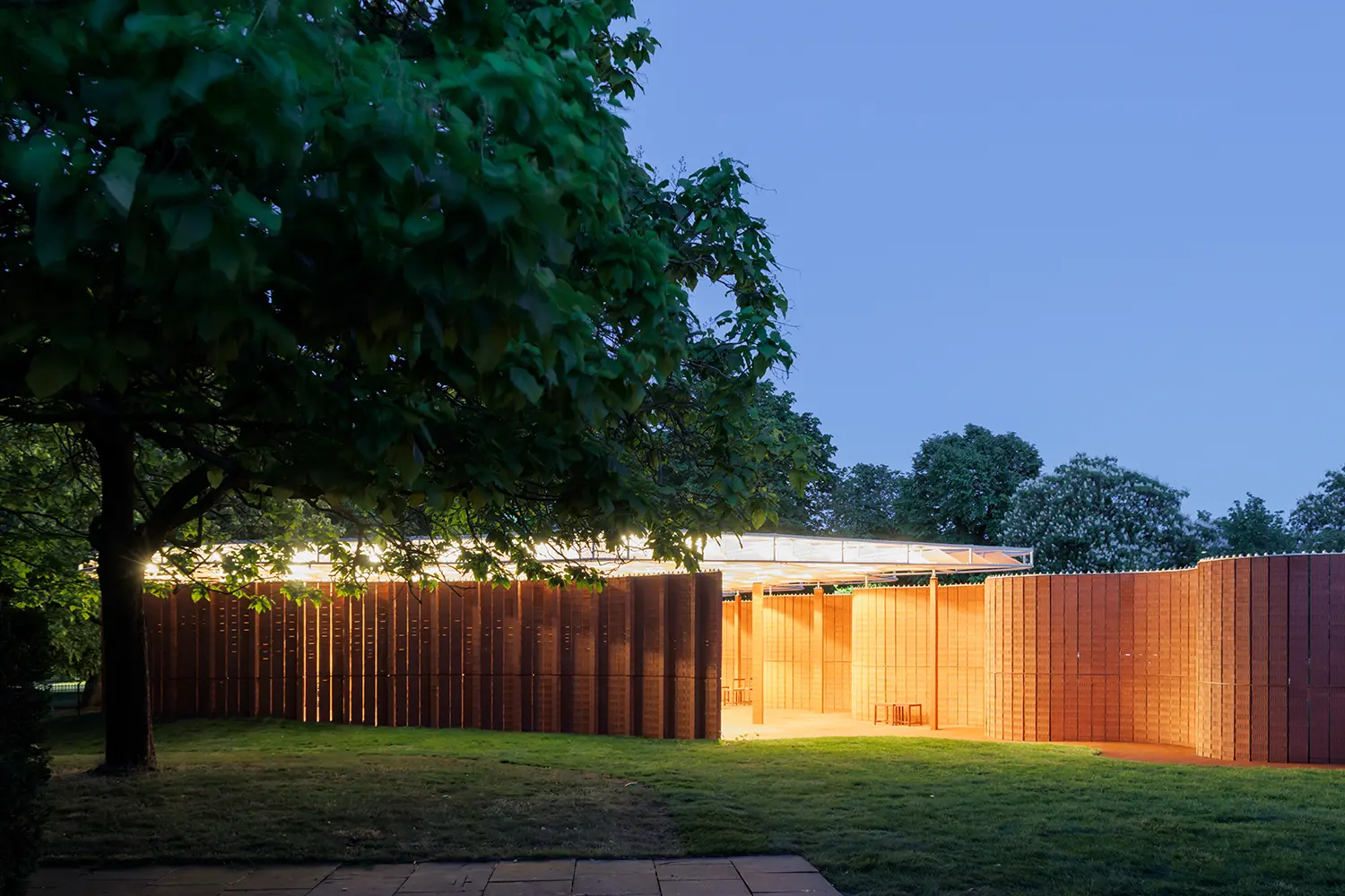 Serpentine Pavilion 2026 by LANZA atelier night view illuminated roof brick wall Kensington Gardens London
