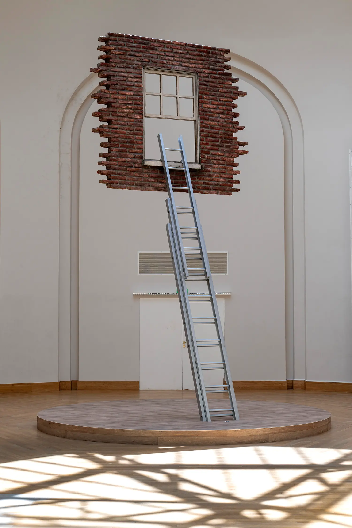 Leandro Erlich installation Grand Palais Paris, suspended brick wall fragment with window, aluminum ladder, circular wooden platform, arched gallery alcove