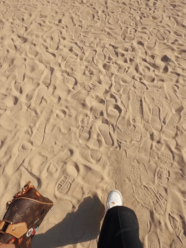 First-person view of a model walking on a sand runway covered in footprints at Louis Vuitton Men's SS27, Paris