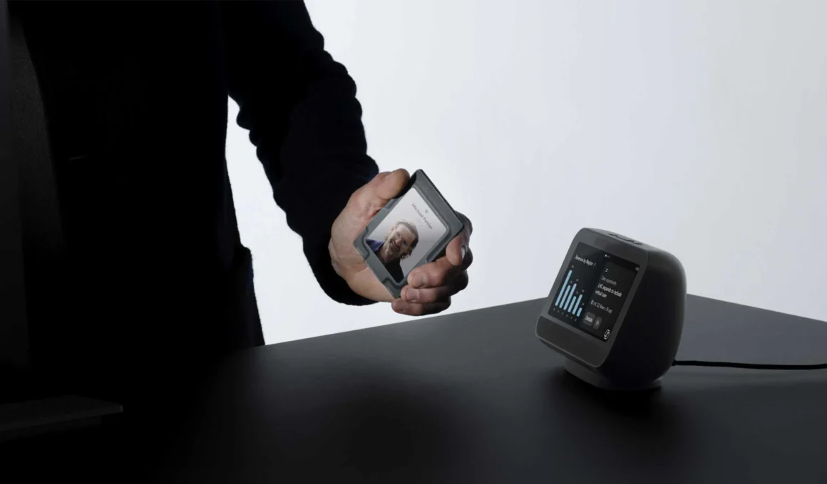 Microsoft Project Solara badge device held in hand next to desk concept dark touchscreen workplace