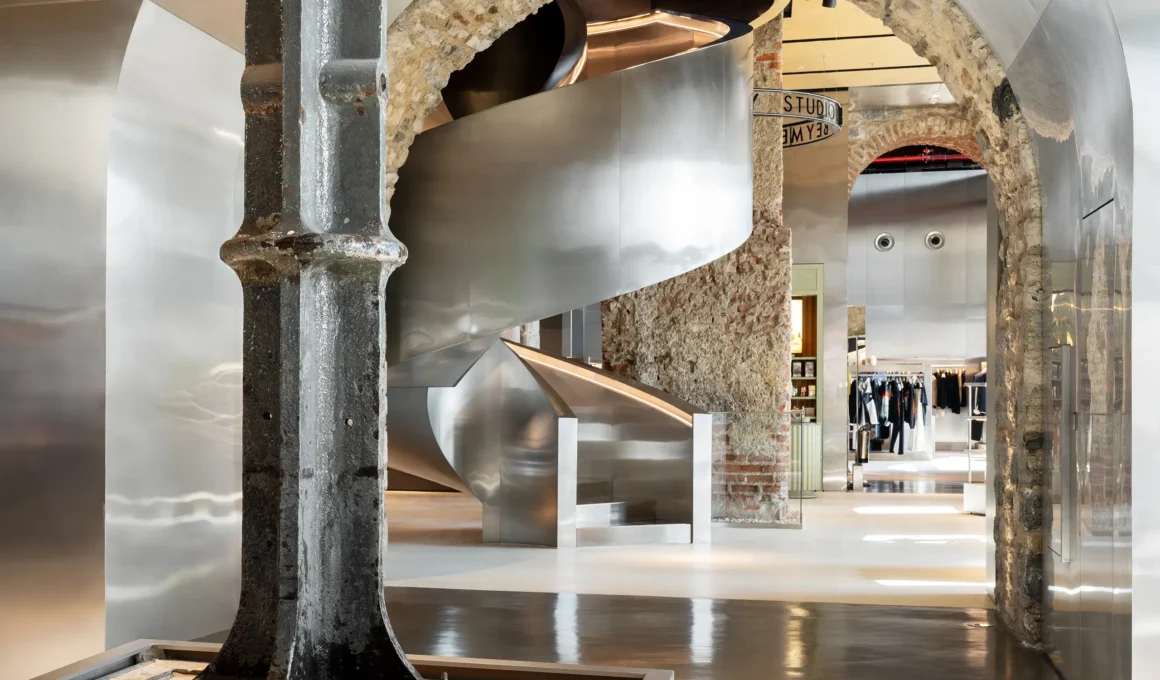 Beymen Tersane OMA Istanbul, polished stainless steel spiral staircase through Ottoman stone arch, original cast iron arsenal column foreground