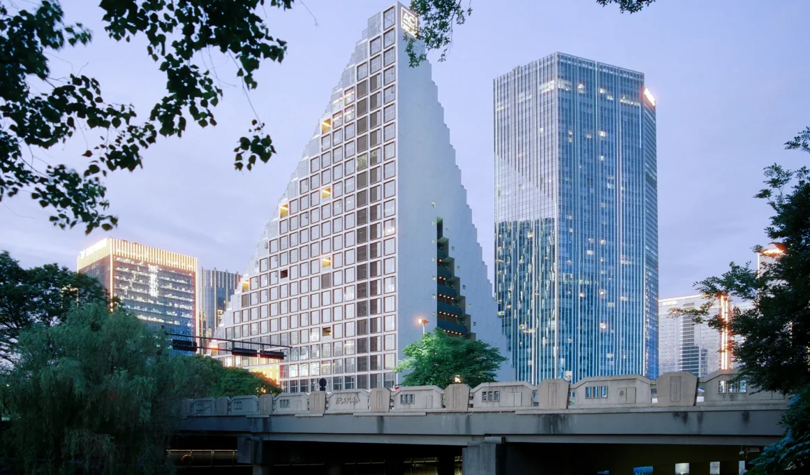 OMA Hangzhou Prism by Chris van Duijn — canal view at dusk showing double oblique cuts through mixed-use volume, surrounding Future Tech City skyline