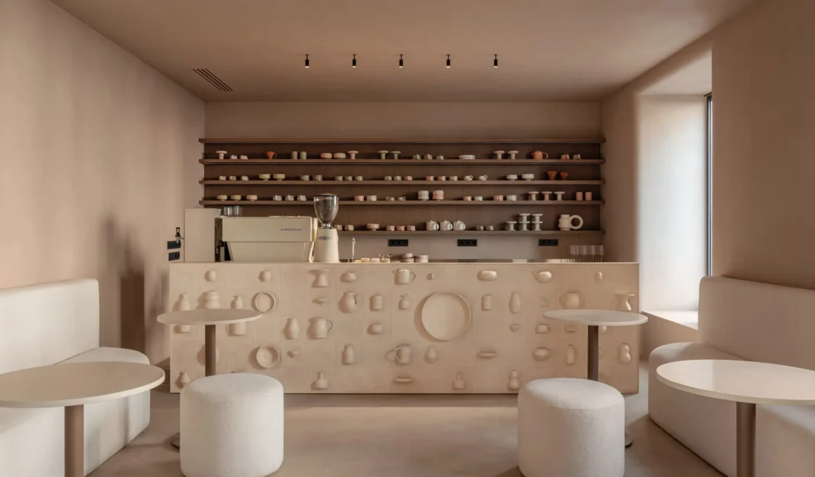 SHOLOMITSKA ceramics store Kyiv by Sivak Partners, café counter clad in custom relief ceramic tile, open shelving with handmade cups and vessels, warm monochromatic interior