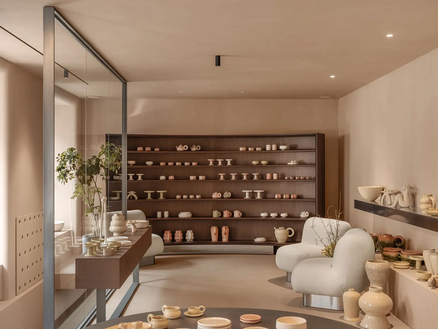 SHOLOMITSKA ceramics store Kyiv, large curved wooden cabinet with ceramic objects on multiple shelves, mirrored partition, bouclé armchair, warm plaster finish