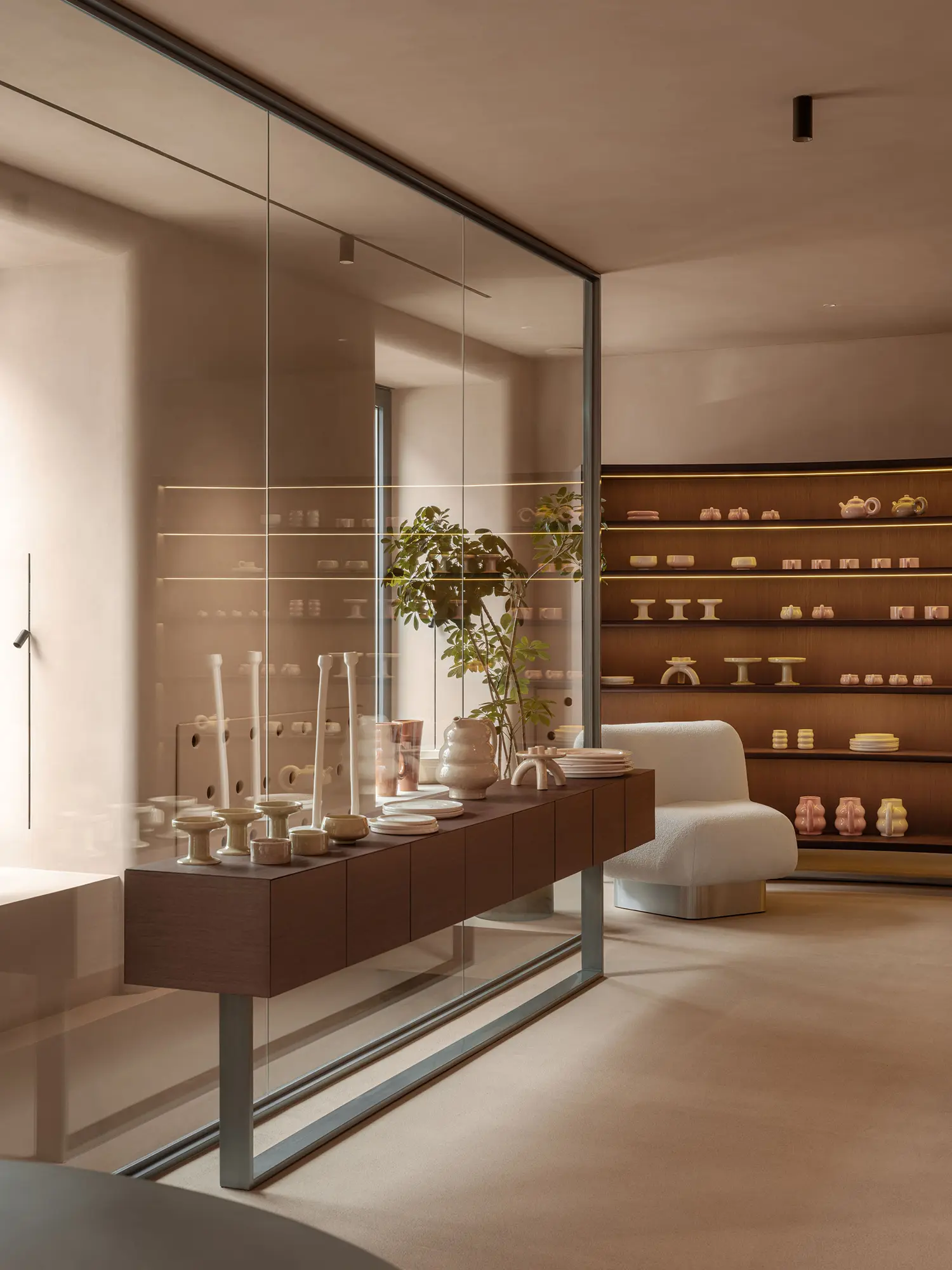 SHOLOMITSKA ceramics store Kyiv by Sivak Partners, glass partition reflecting ceramic display shelves with integrated LED strip lighting, dark wood joinery, bouclé seating