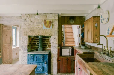 Kitchen at Purbeck Cottage by TYPE, restored blue cast-iron stove built into Purbeck stone chimney breast, reclaimed pine cabinetry, salvaged stone sink with brass taps