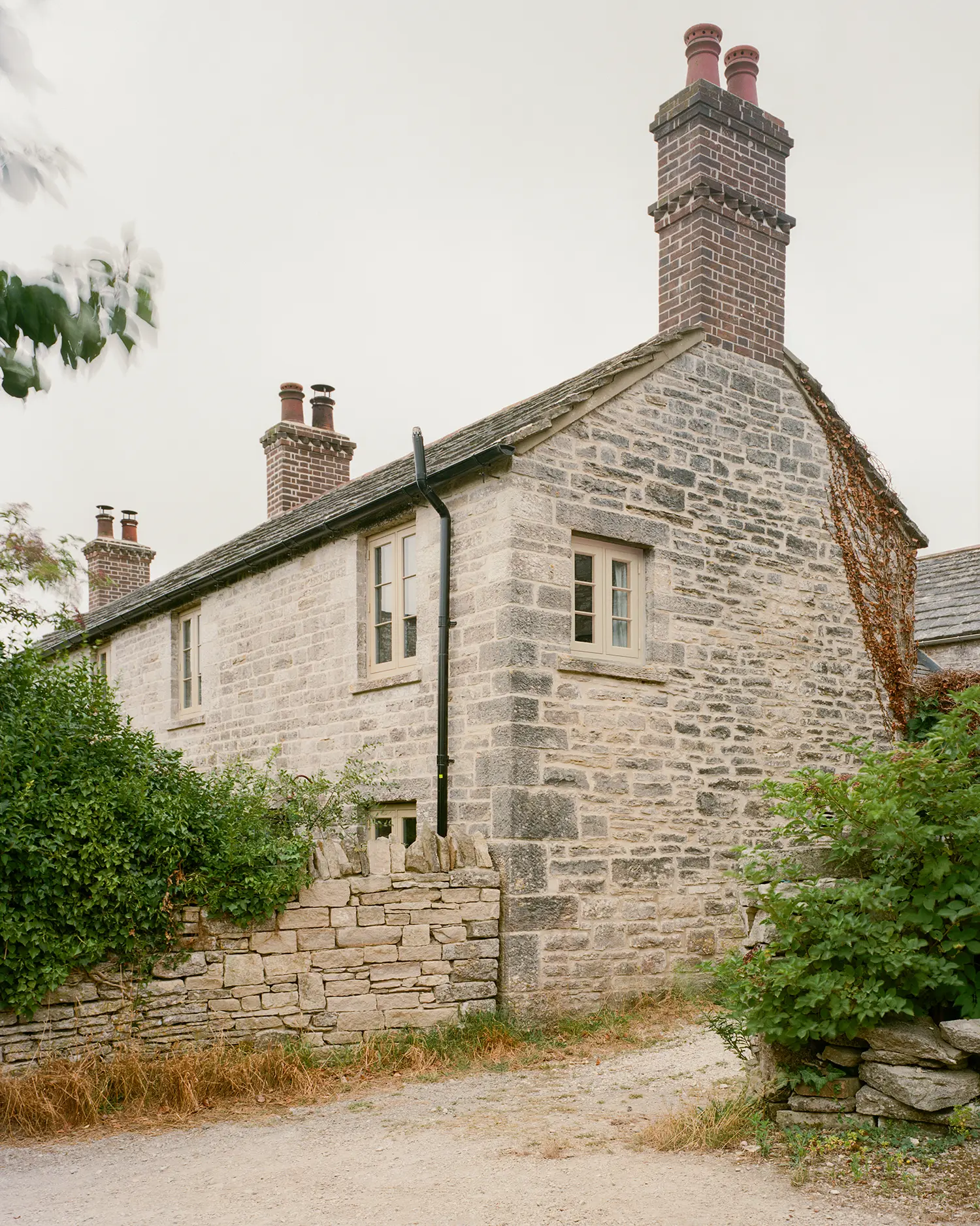 Exterior of Purbeck Cottage by TYPE on the Isle of Purbeck, Dorset, dressed stone facade with twin brick chimney stacks and restored timber windows