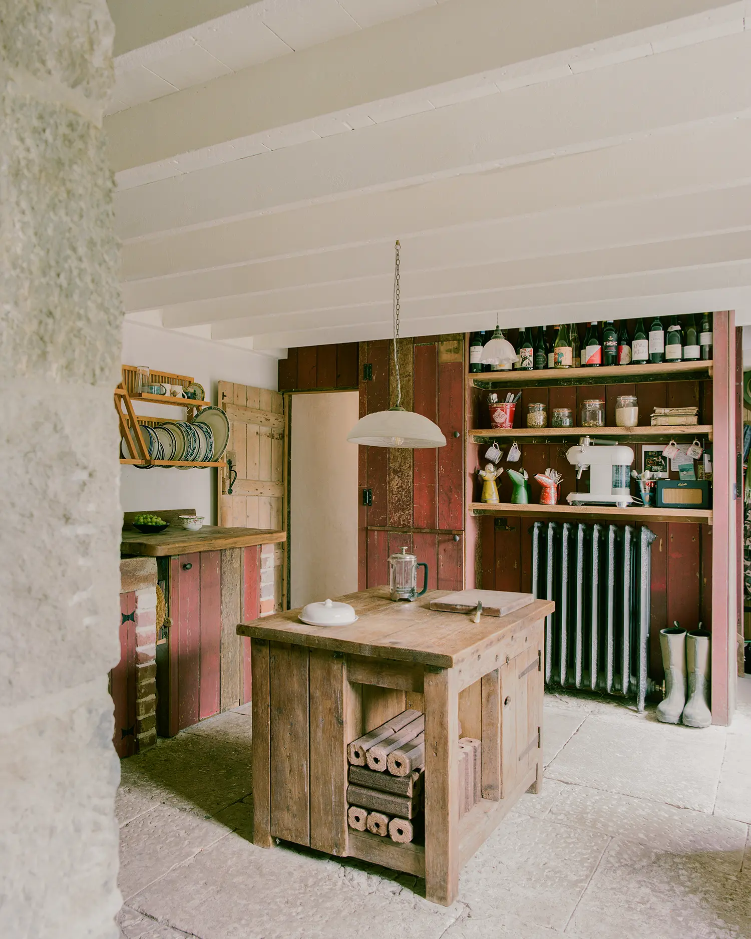 Kitchen at Purbeck Cottage by TYPE, freestanding reclaimed timber island with built-in log storage, salvaged red-painted cabinetry, cast-iron radiator