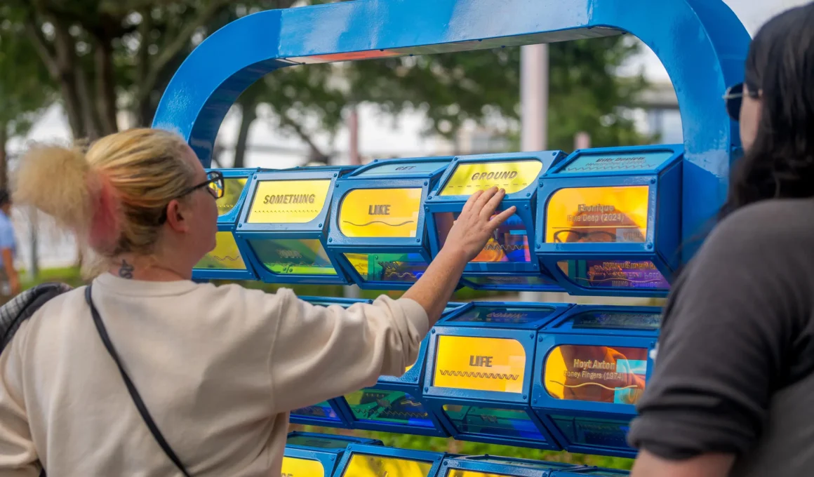 A Cappella interactive public art installation Jacksonville, visitor rearranging dichroic lyric panels with words Something Like Ground Life, St Johns River background