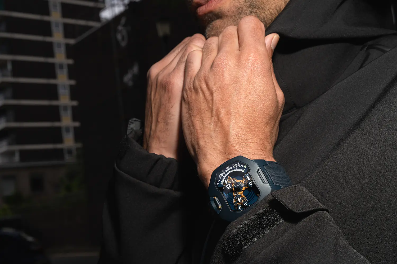 URWERK UR-120 Blue Planet lifestyle shot on wrist, sandblasted blue steel case, urban construction background, dark jacket