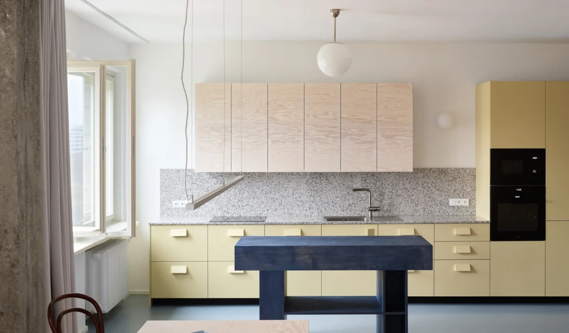 Prokop Hartl Prague kitchen, pale celery cabinets, pink plywood uppers, navy solid-wood island, granite worktop, blue resin floor, concrete beam