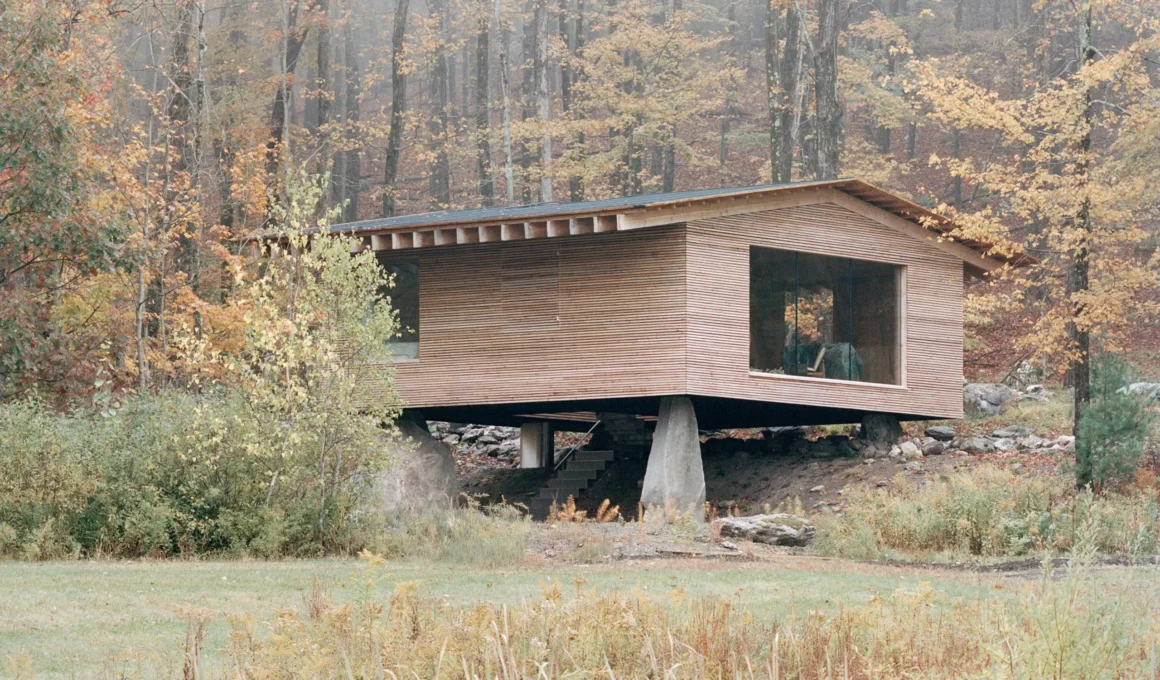 The Findling by Of Possible in Austerlitz, New York, larch-clad cabin raised on a concrete pier above a stone stair in autumn forest
