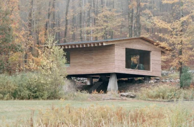 The Findling by Of Possible in Austerlitz, New York, larch-clad cabin raised on a concrete pier above a stone stair in autumn forest