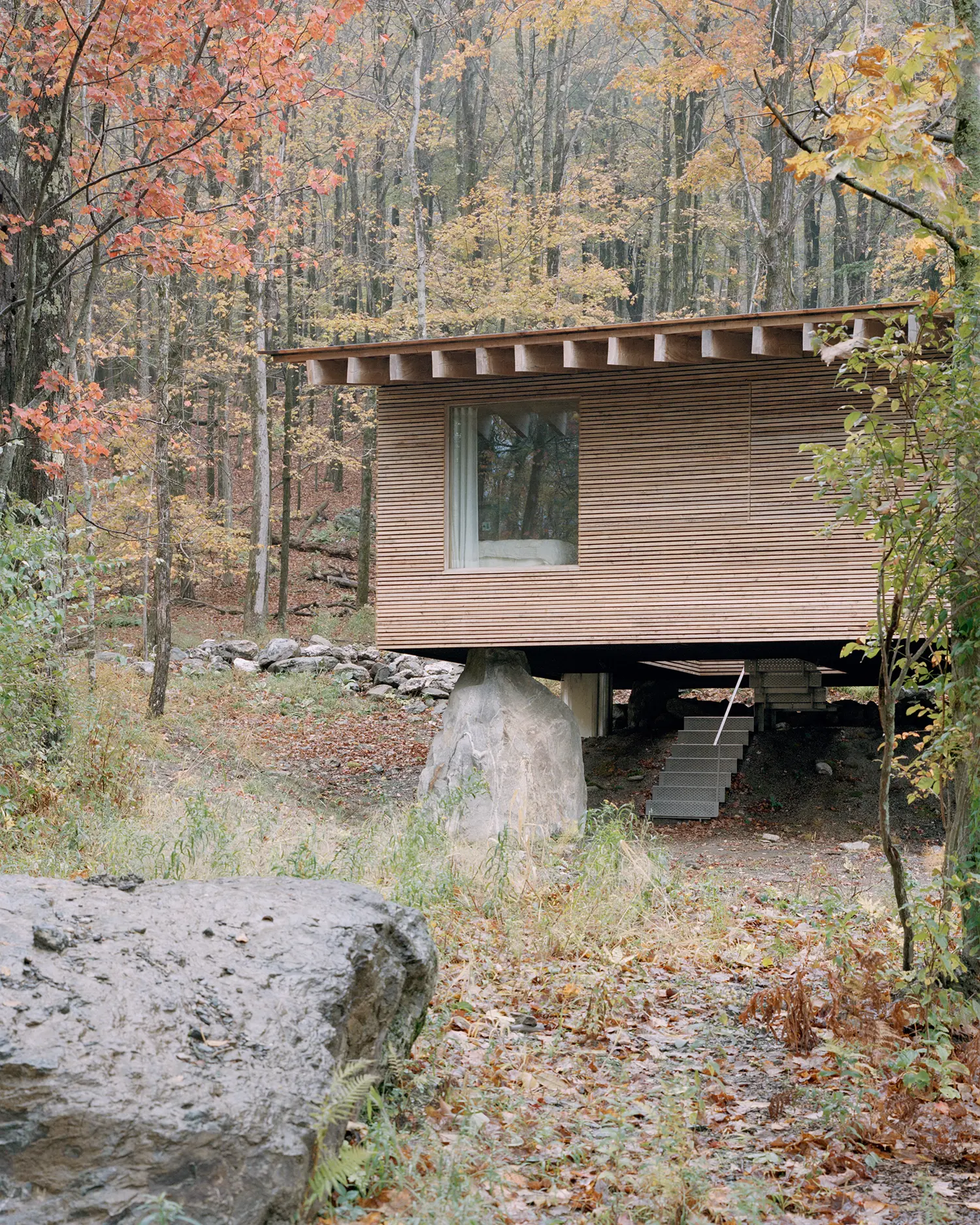 The Findling by Of Possible, larch cabin resting on a glacial erratic boulder with a perforated steel stair visible beneath
