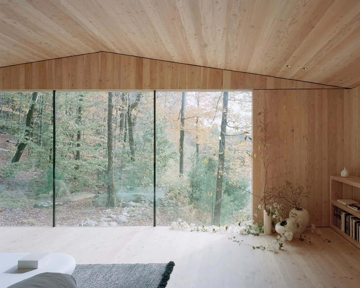 Interior of The Findling by Of Possible, floor-to-ceiling glass corner in a larch-lined bedroom facing dense autumn forest