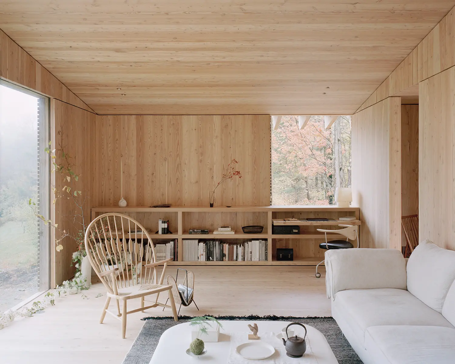 Living area of The Findling by Of Possible, larch-paneled walls, built-in shelving, Windsor chair and floor-to-ceiling window