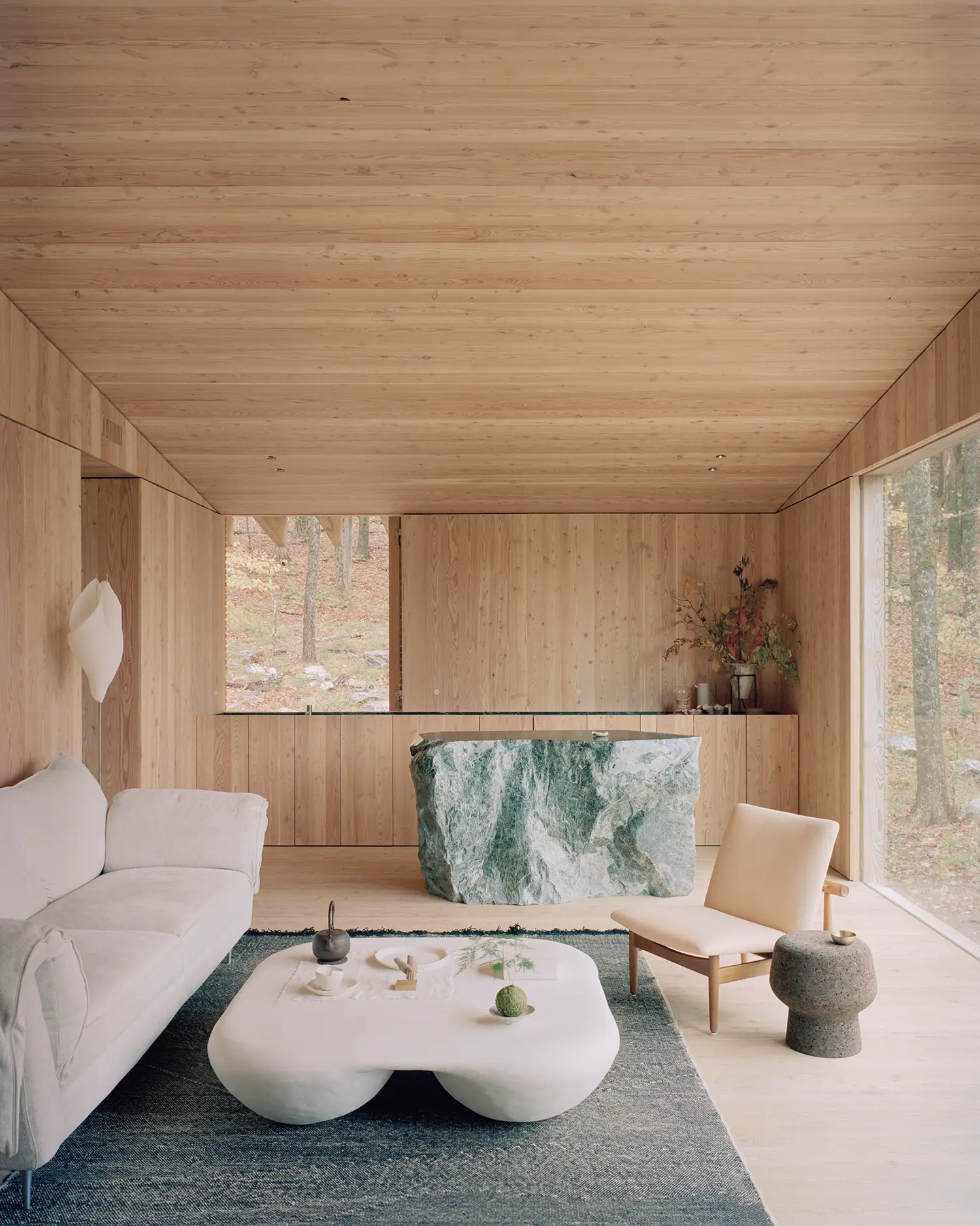 Kitchen island in The Findling by Of Possible, unpolished Vermont Verde serpentine block set against larch cabinetry and forest view