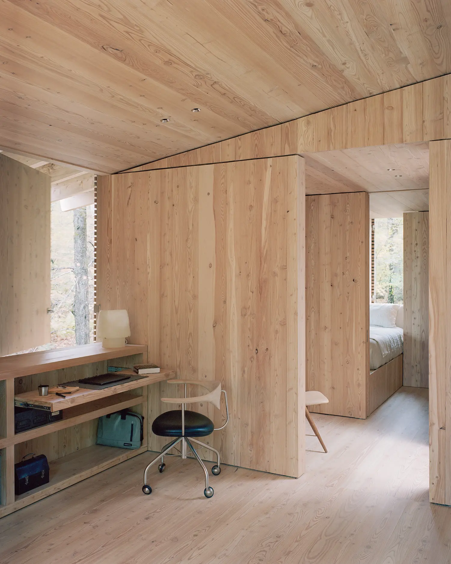 Hallway and study nook in The Findling by Of Possible, larch-clad walls with built-in desk, office chair, and bedroom beyond