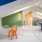 Attic apartment at night by gon architects, orange sculptural chair, mirrored wall reflecting living room beyond