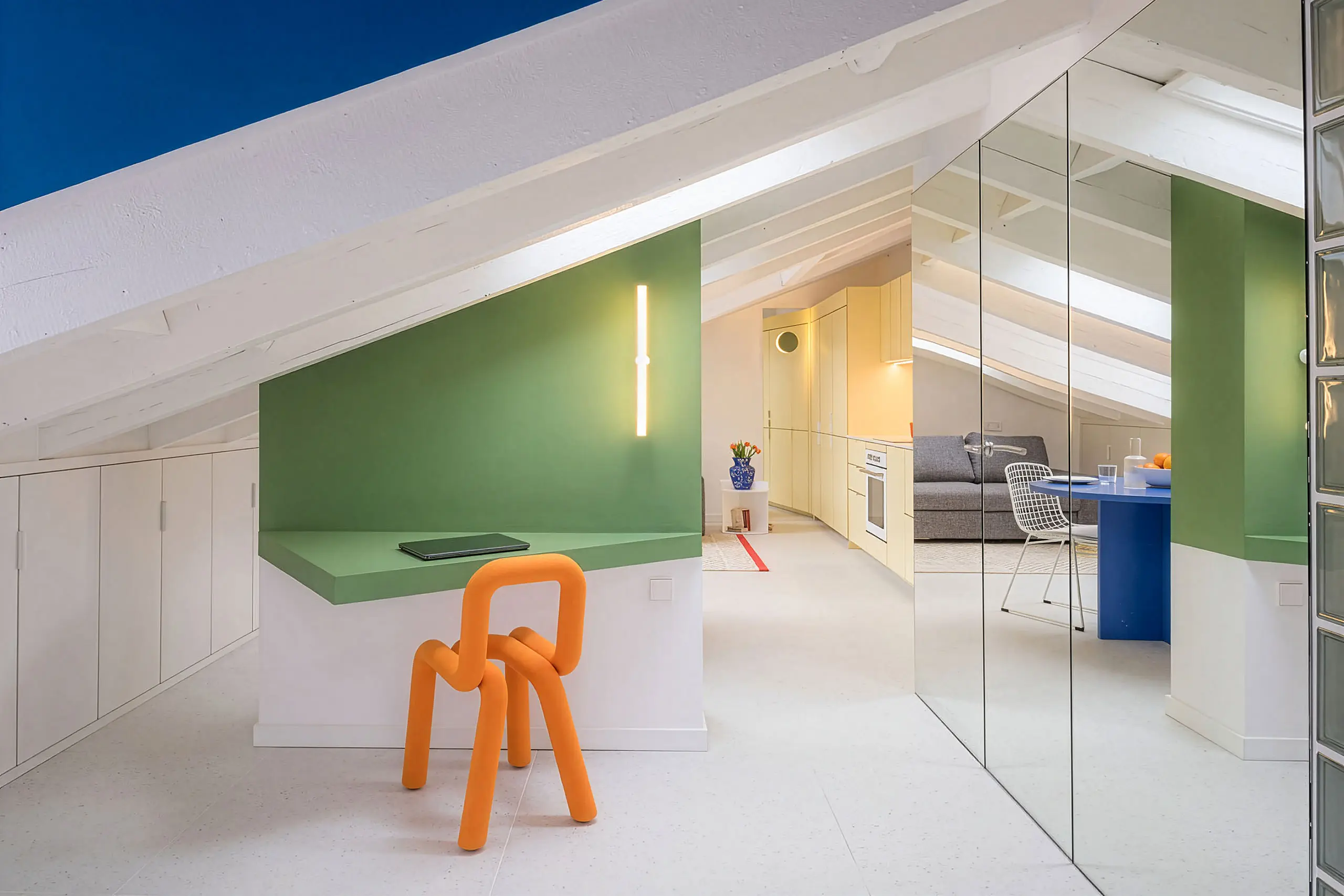 Attic apartment at night by gon architects, orange sculptural chair, mirrored wall reflecting living room beyond