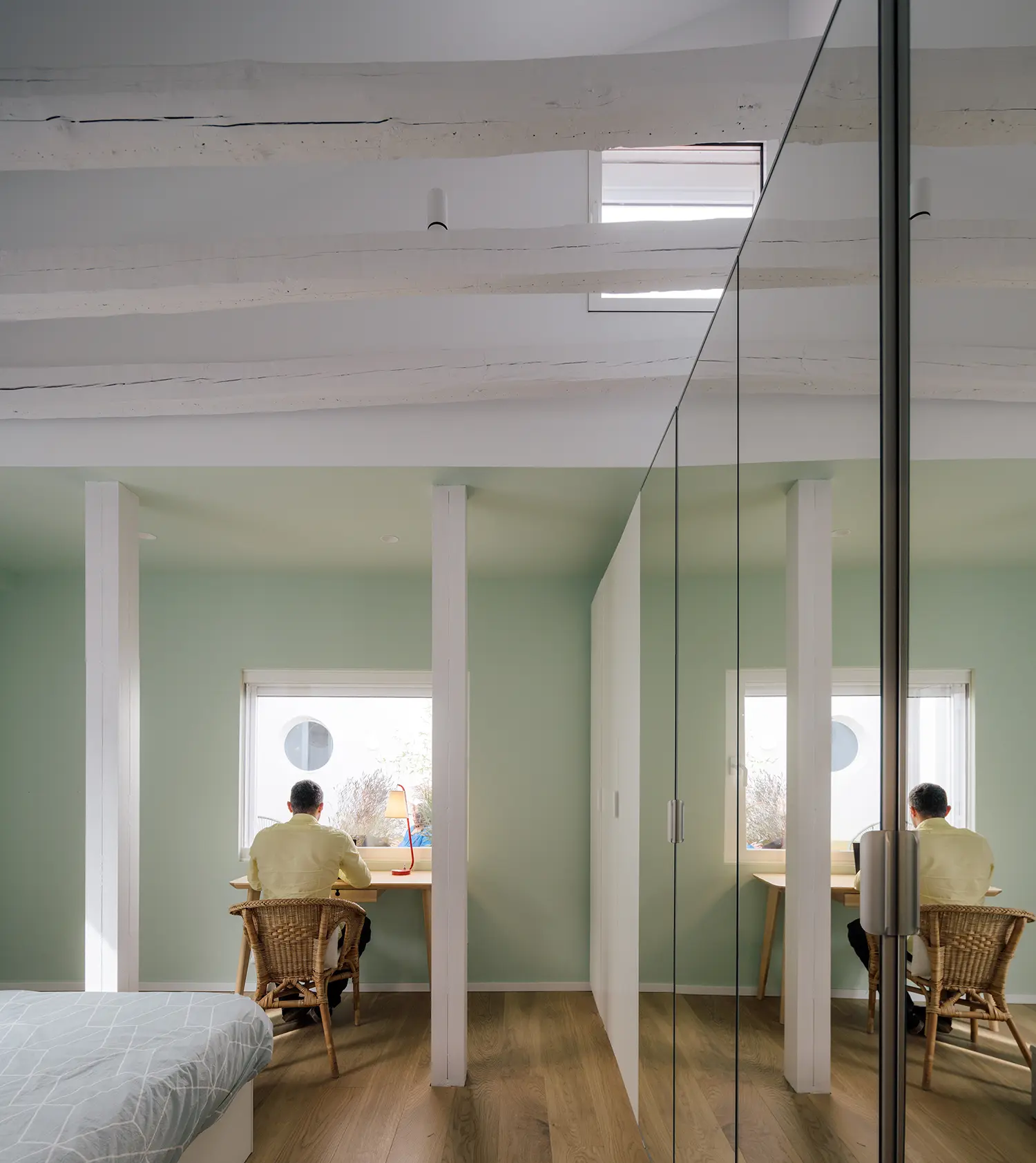 Attic home office with mirrored partition wall, wicker chair, wooden desk, sage green interior