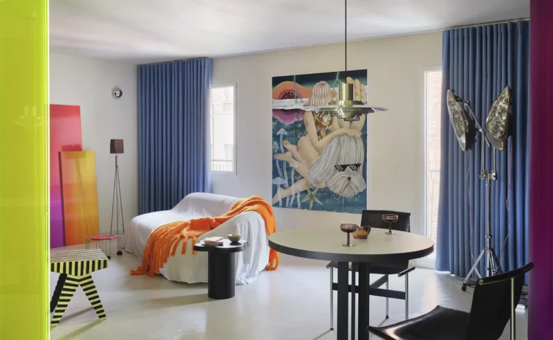 Macedonia apartment by Bardo, Madrid — living and dining area with neon acrylic threshold, blue curtains, and vintage artwork