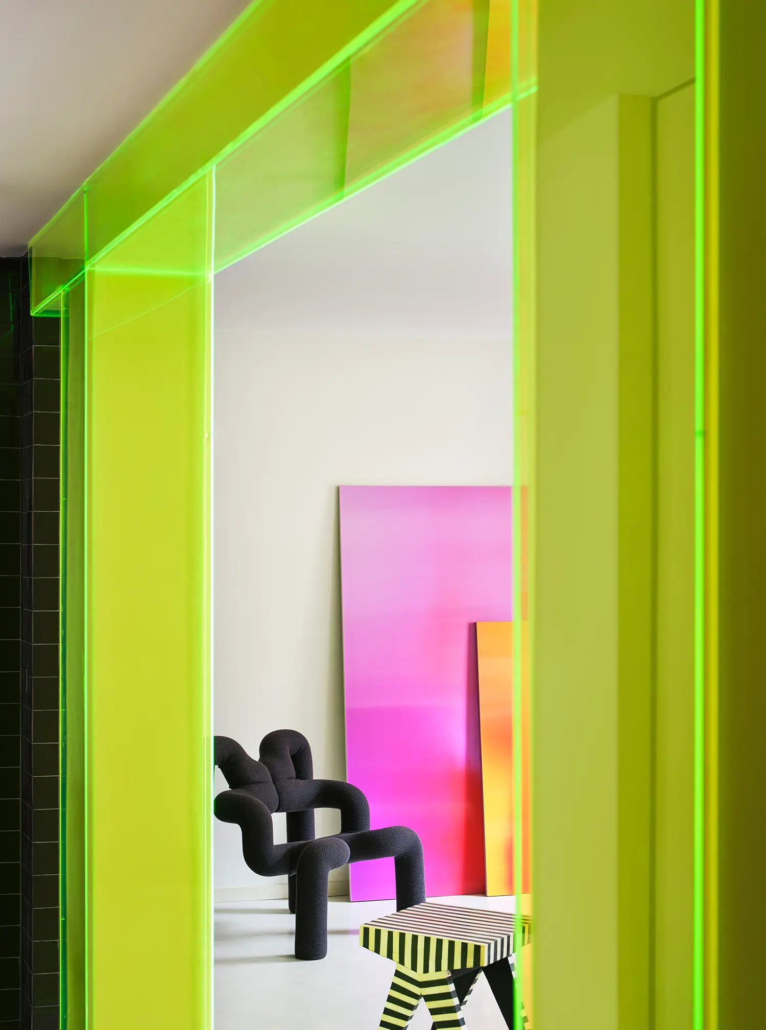 Macedonia by Bardo, close-up of neon acrylic column cladding framing living room with black armchair and gradient paintings