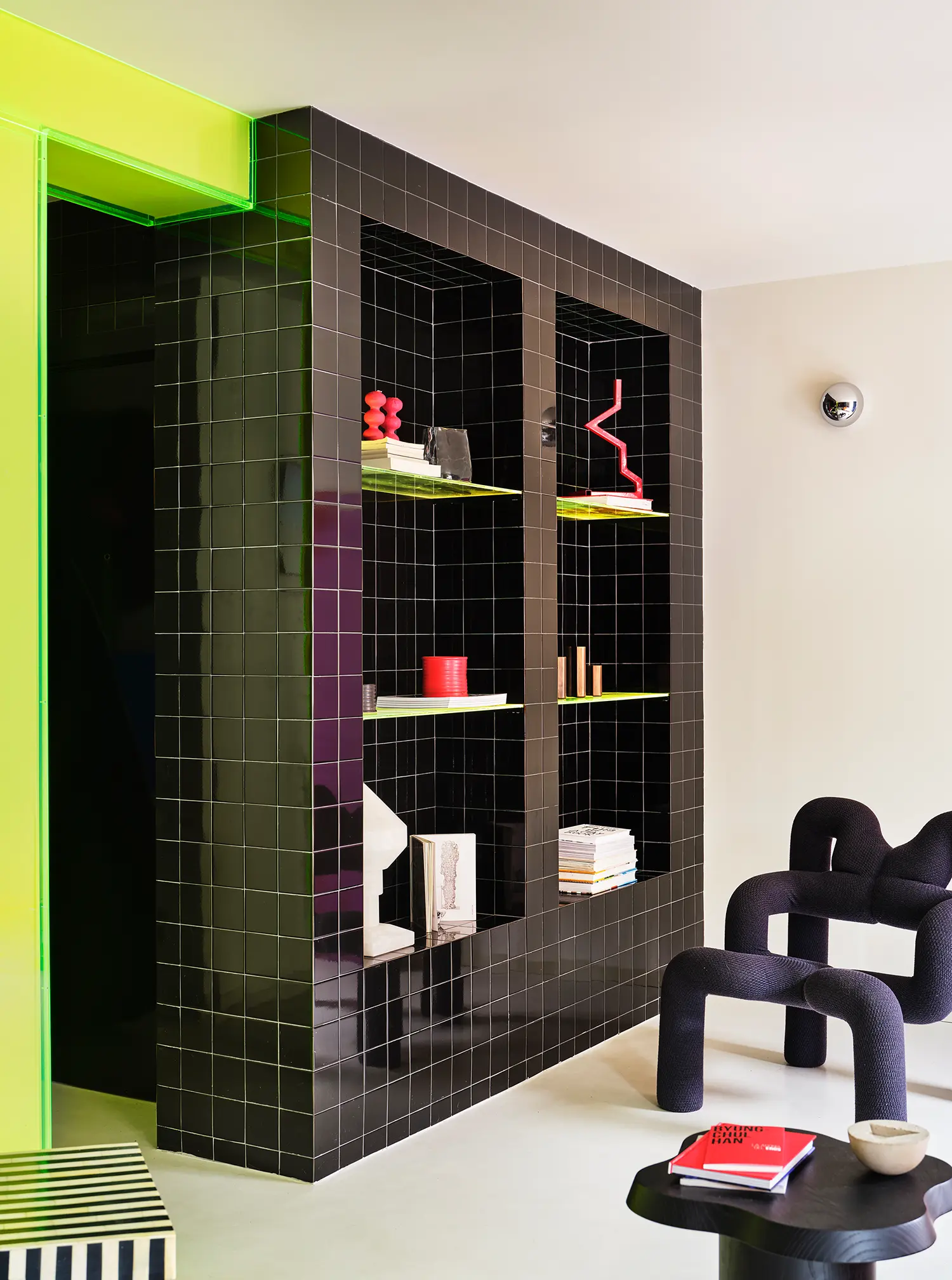 Macedonia by Bardo, black tiled shelving unit with neon-edged niches, sculptural objects, and books