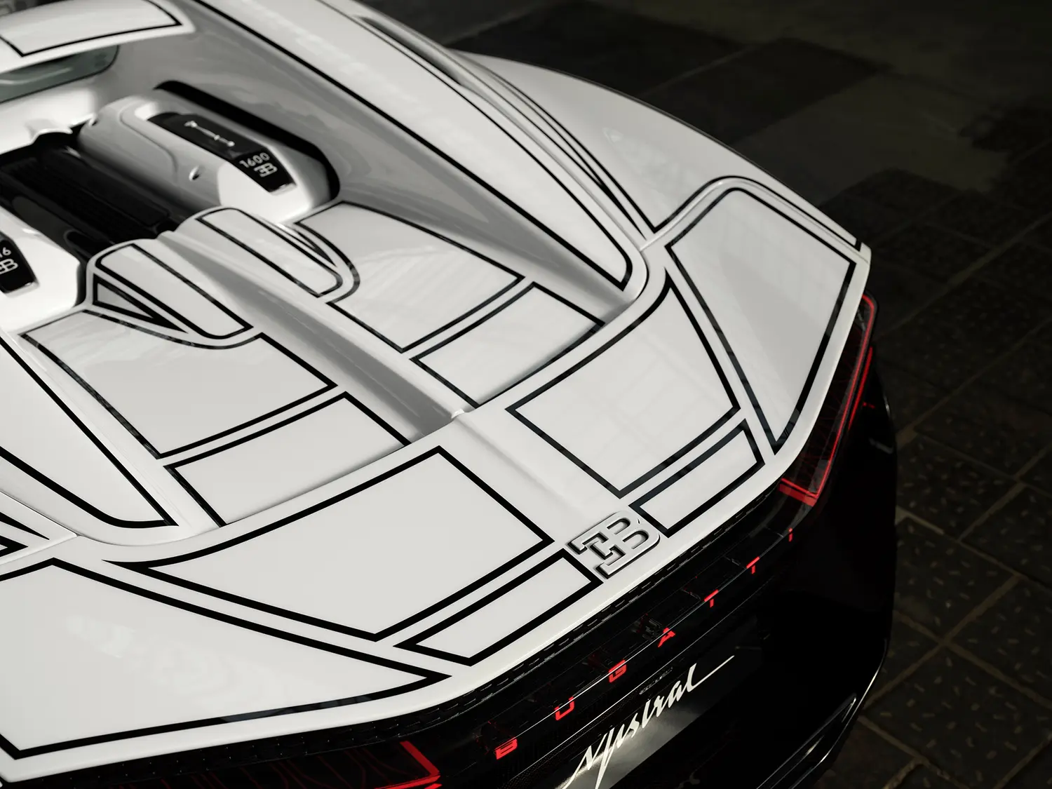 Bugatti W16 Mistral 'Blanc Éternel', close-up rear deck detail, EB emblem and black line graphic converging above illuminated taillights