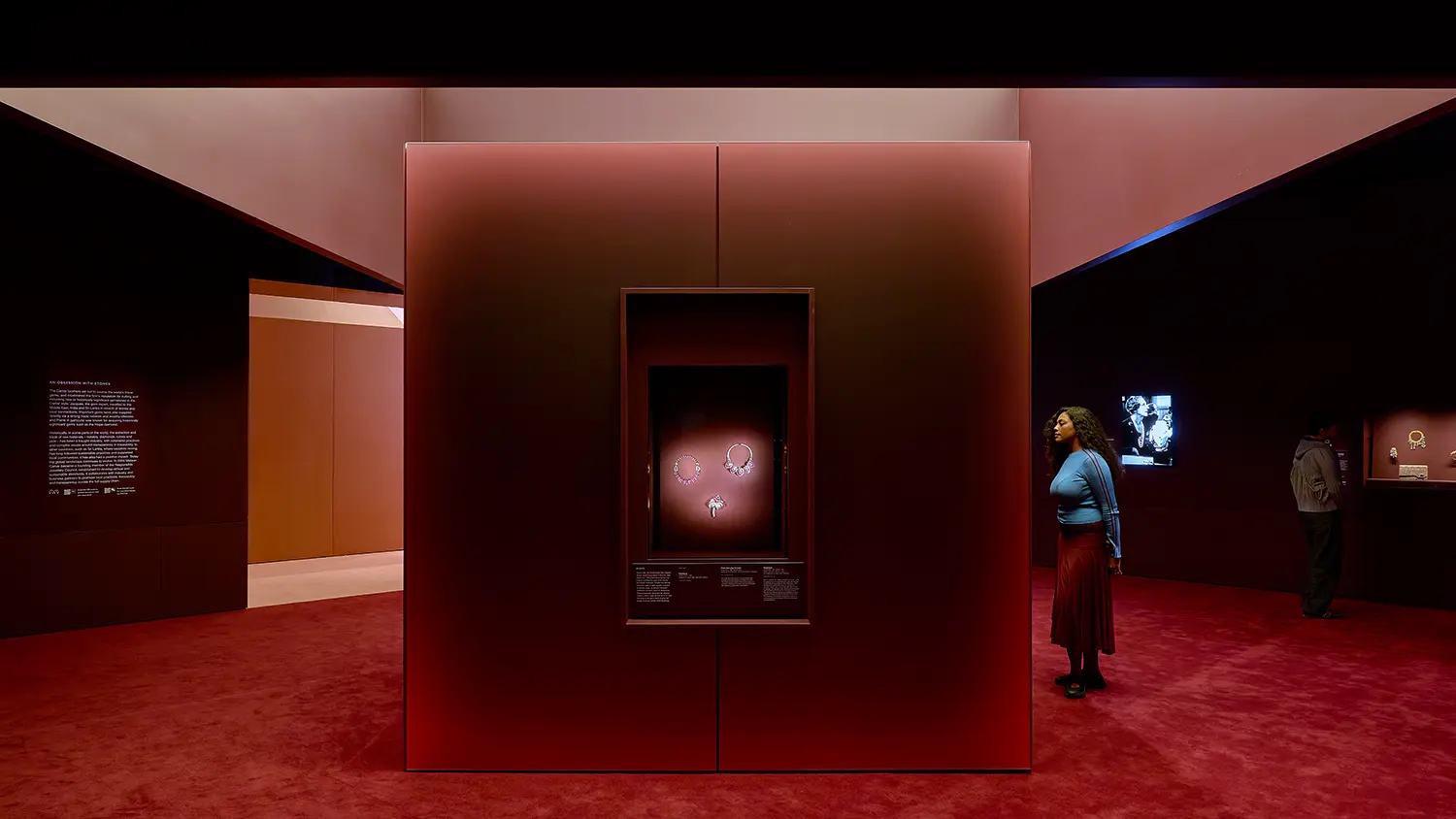 CARTIER at NGV Melbourne: deep red gallery with freestanding display monolith holding illuminated jewelry under a dark ceiling